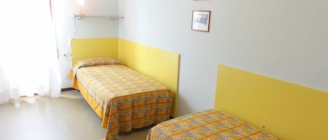 A room with two beds, each with a patterned bedspread. There are three framed pictures on the wall.