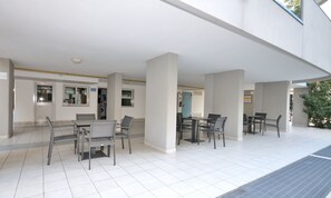 Un espace extérieur moderne aménagé avec des tables et des chaises, une allée couverte et une vue sur l’intérieur du bâtiment.