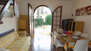 Un comedor con una mesa dispuesta para cuatro, un sofá y vista al jardín a través de un arco abierto.