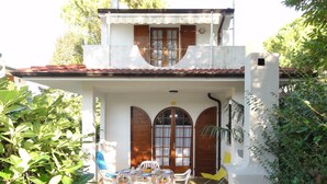 Un edificio de dos pisos con techo de tejas, un balcón y un patio cubierto con mesa y sillas.