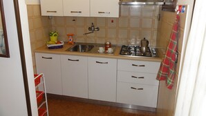 Una cocina compacta con armarios blancos, un lavamanos de acero inoxidable y una estufa a gas.