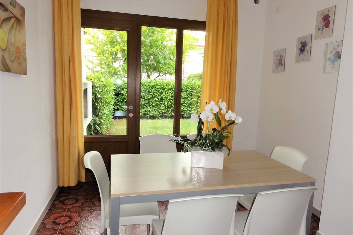A dining area with a table, chairs, a potted plant, and a view of greenery outside.