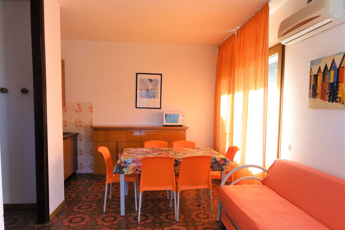A compact room with a dining table, orange chairs, a sofa, and a microwave.