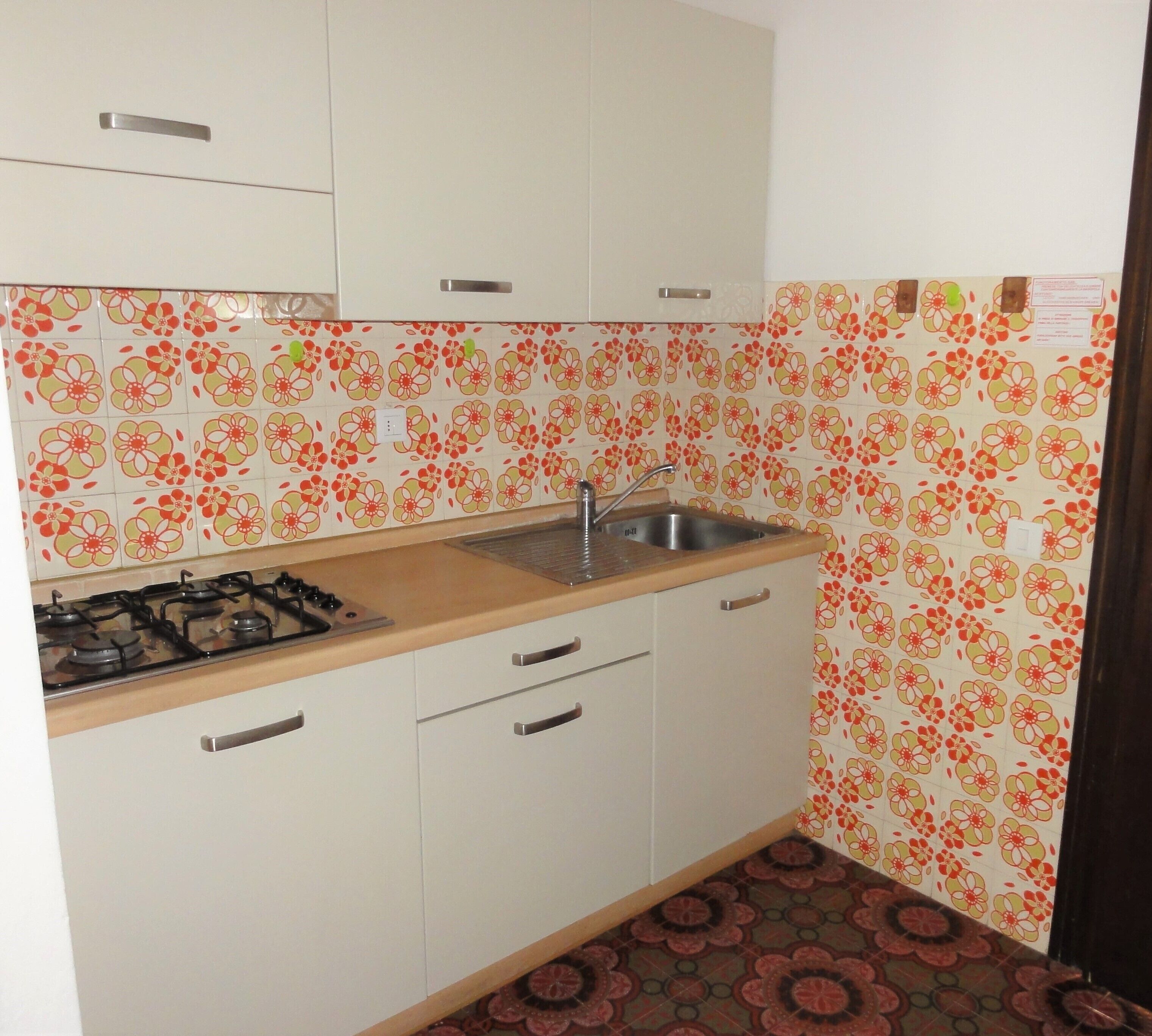 Een kleine keuken met witte kastjes, een roestvrijstalen spoelbak en een gasfornuis.
