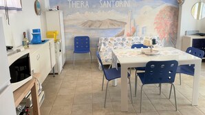 A dining area with a mural of a coastal scene, a table with chairs, and a refrigerator. - Villa Auriga (San Michele al Tagliamento)