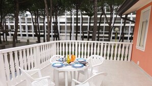 A balcony with a white railing, a round table with white chairs, and a view of a building with multiple floors in the background. - Villa Auriga (San Michele al Tagliamento)