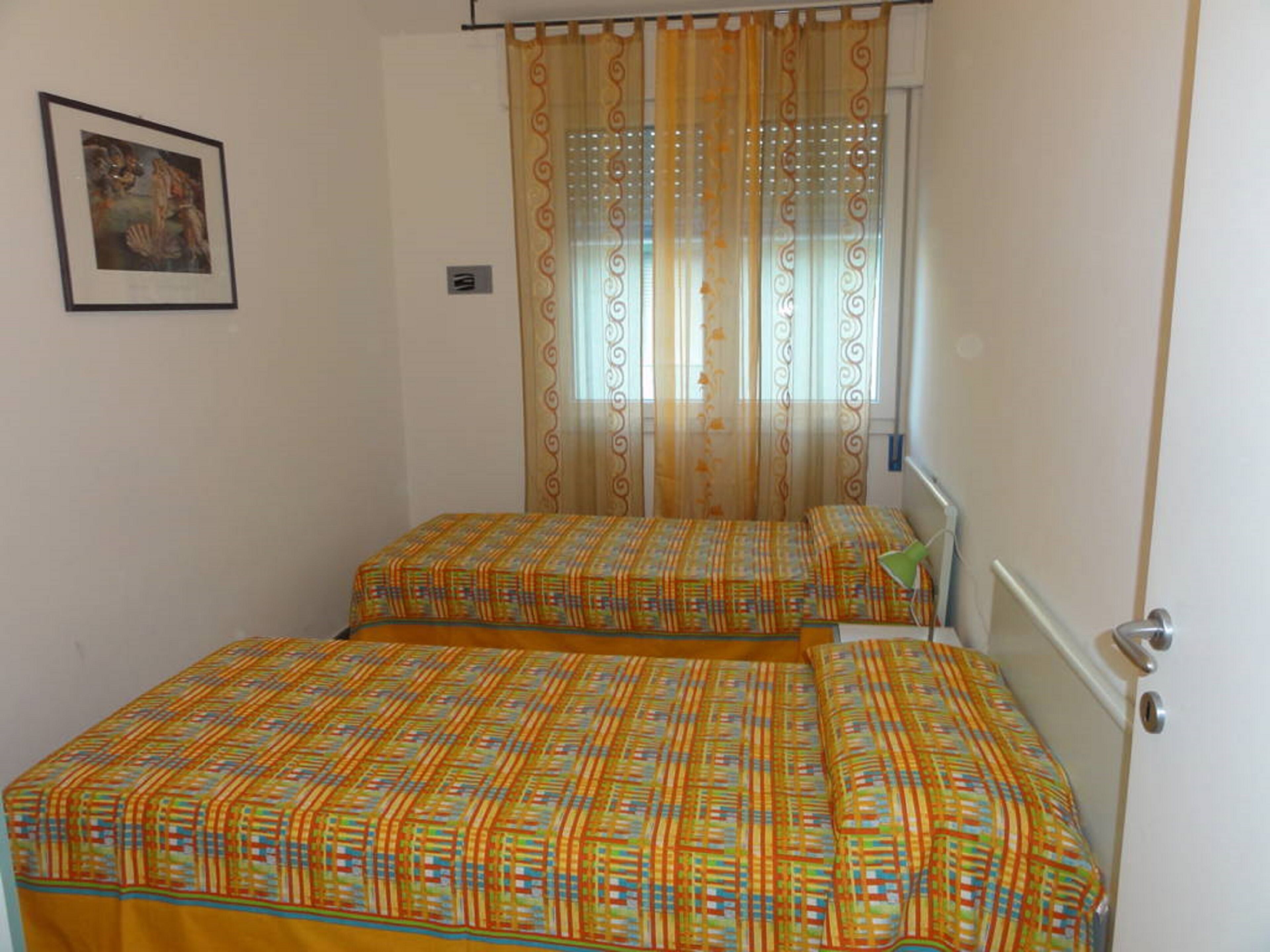 A room with two beds, a window with curtains, a door, and a framed picture on the wall.