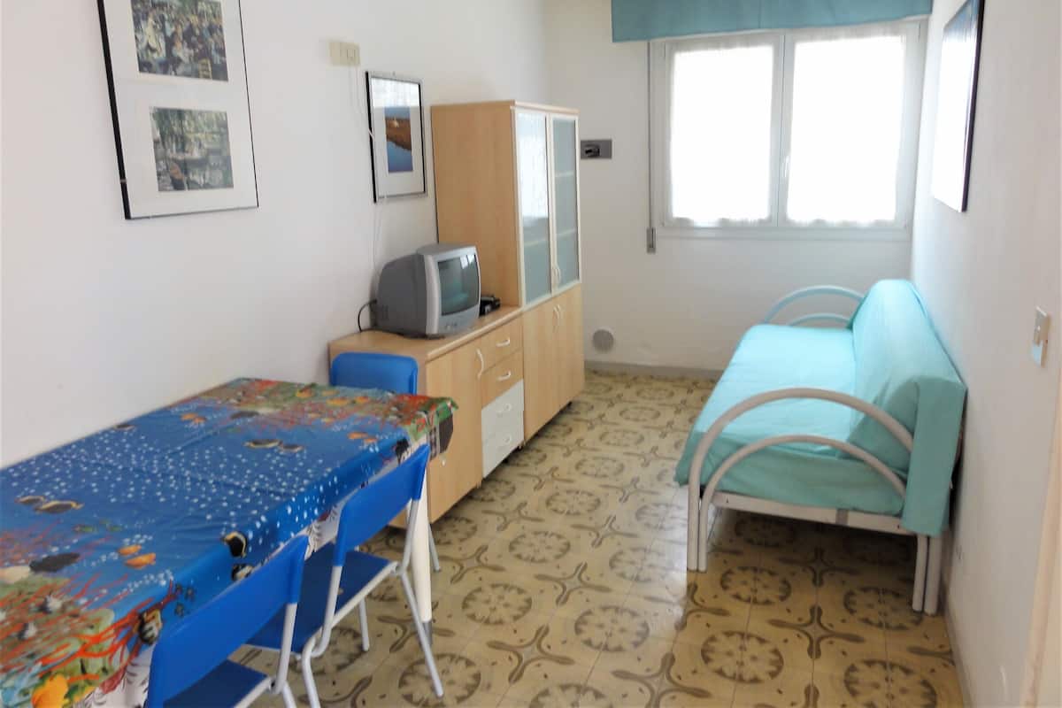 Ein Zimmer mit Bett, Schreibtisch, Stuhl, Fernseher und Fenster.