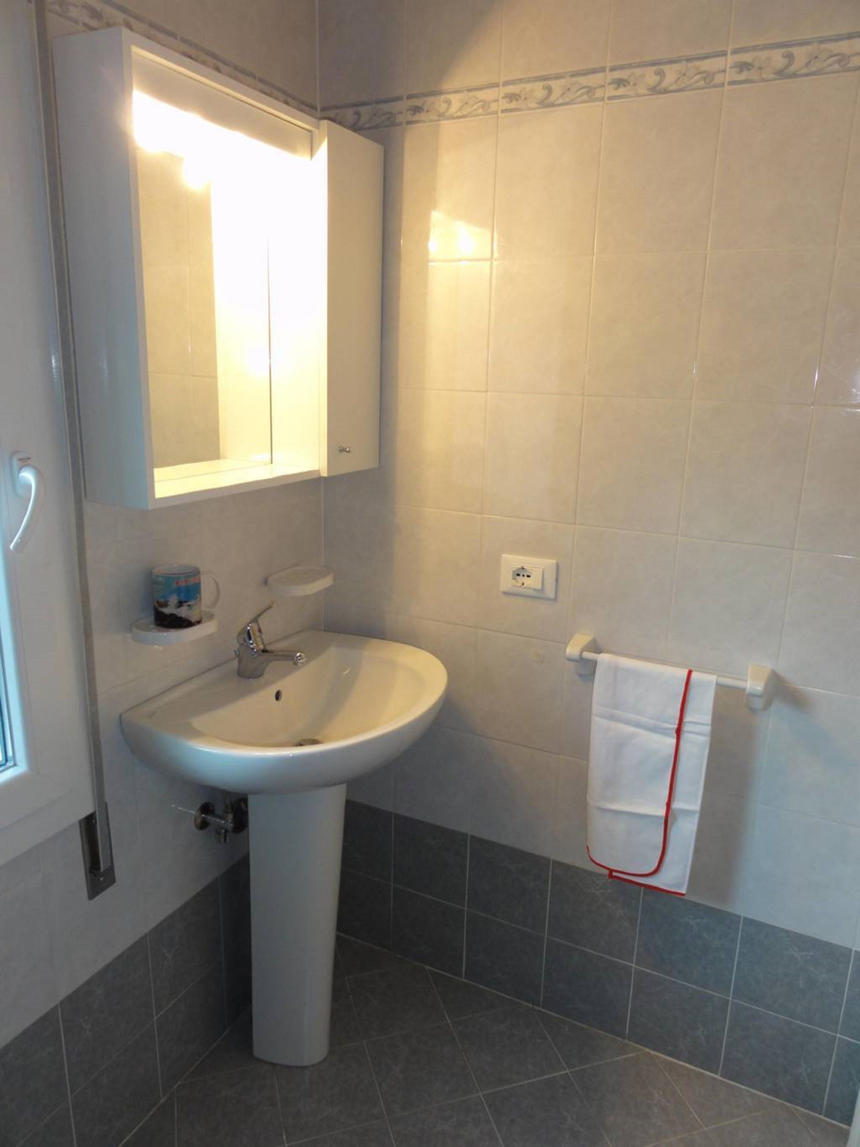 Un baño con lavamanos pedestal, un espejo y un perchero para toallas.
