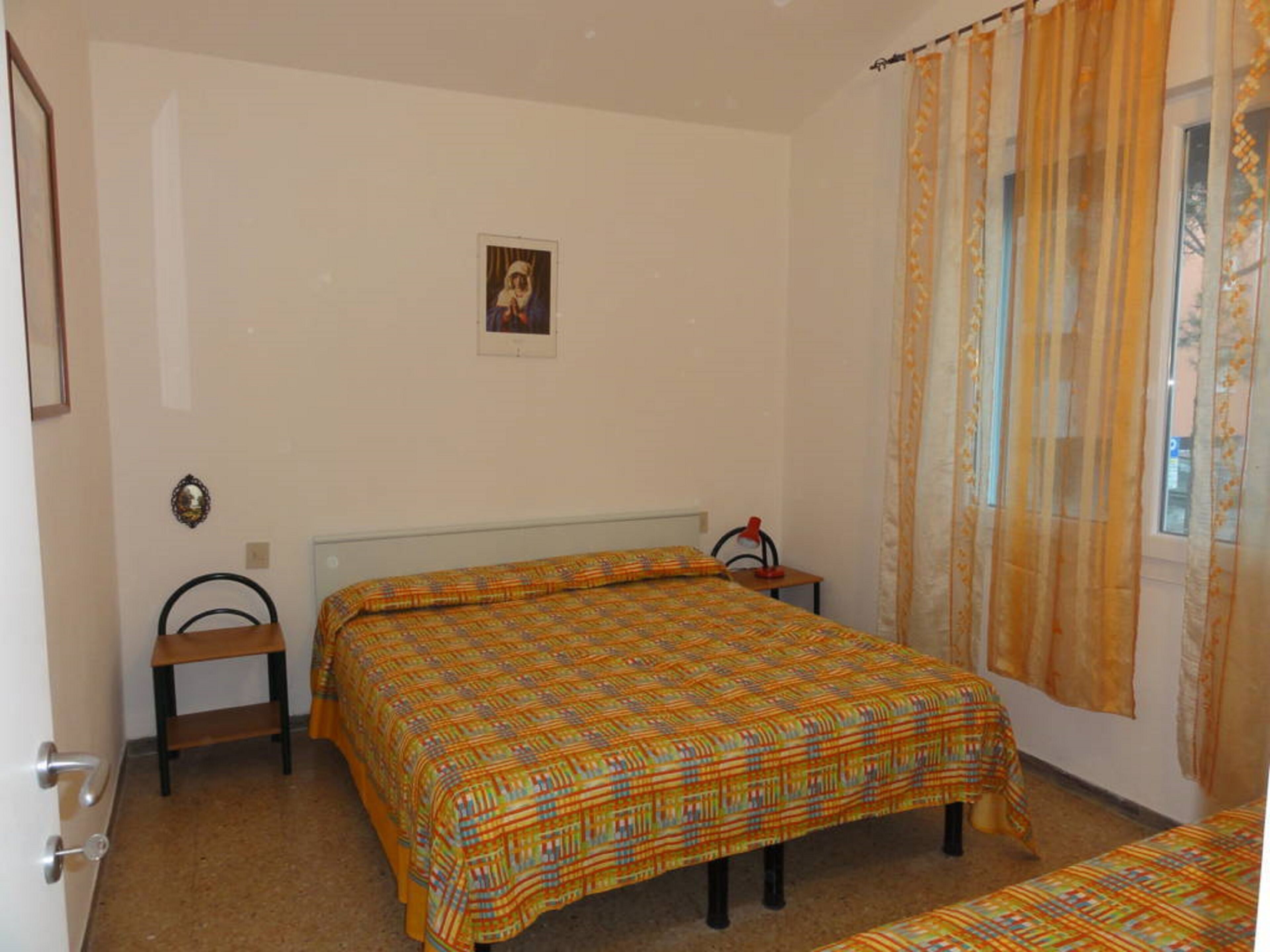 A bedroom with two single beds, a small bedside table with a lamp, a framed picture on the wall, and a window with curtains.