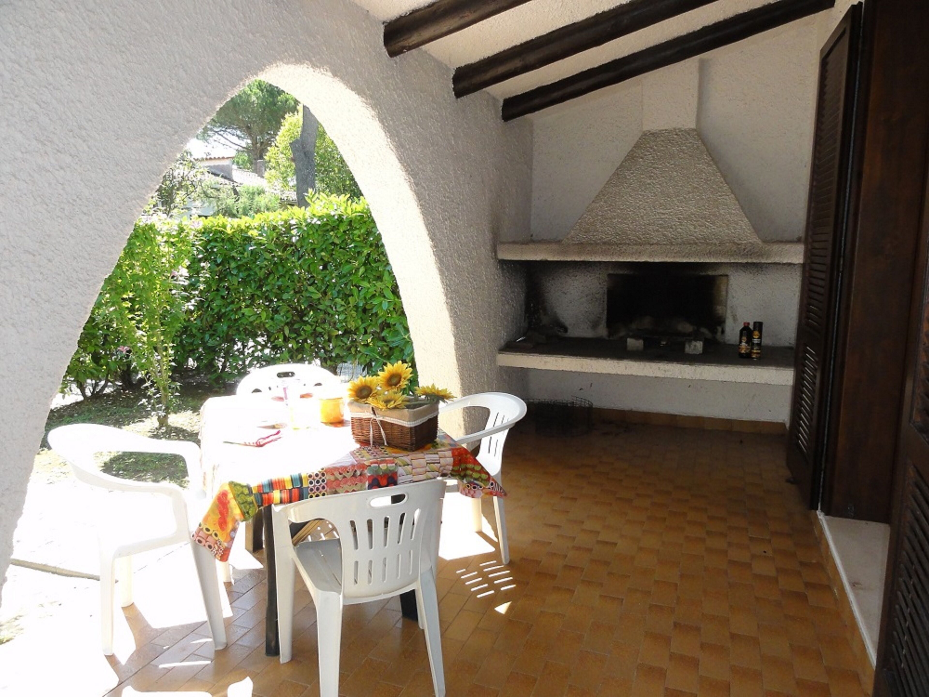 Eine Terrasse im Freien mit einem Esstisch, umgeben von weißen Stühlen, einem Grill und einem Korb Sonnenblumen.