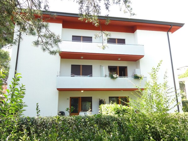 A multi-story building with balconies and a garden area in front.