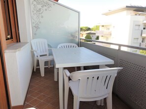 A balcony with a white table and chairs, a frosted glass partition, and a view of buildings in the background.
