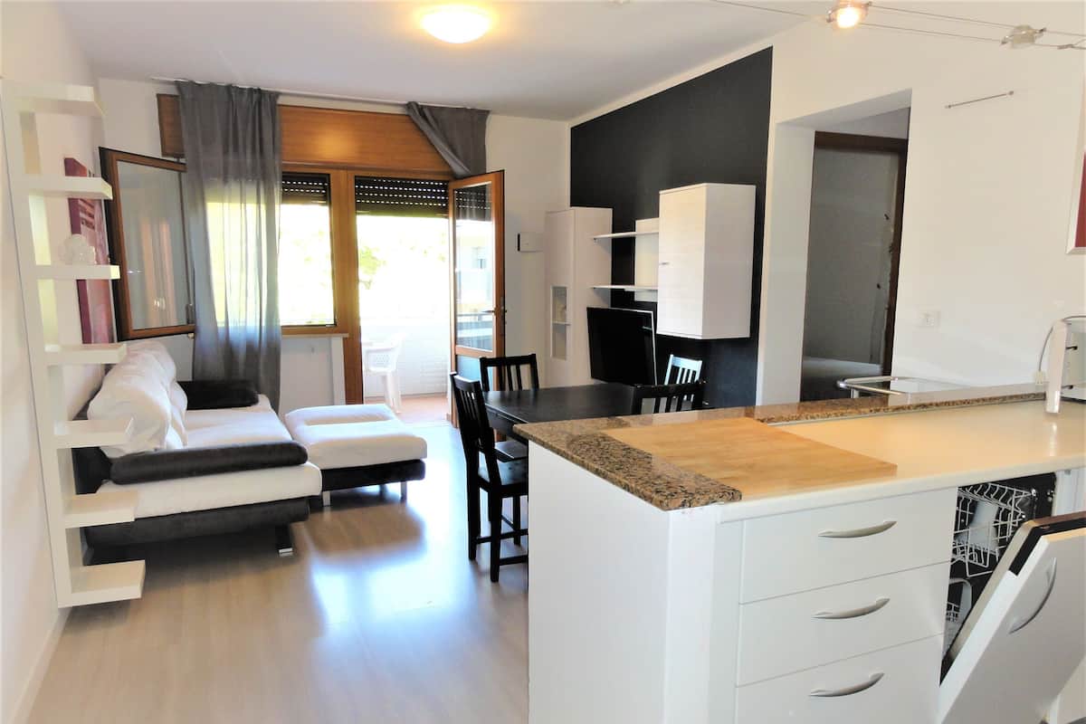 Uma cozinha moderna com armários brancos, bancada de madeira e um espaço de refeições com mesa e cadeiras brancas.