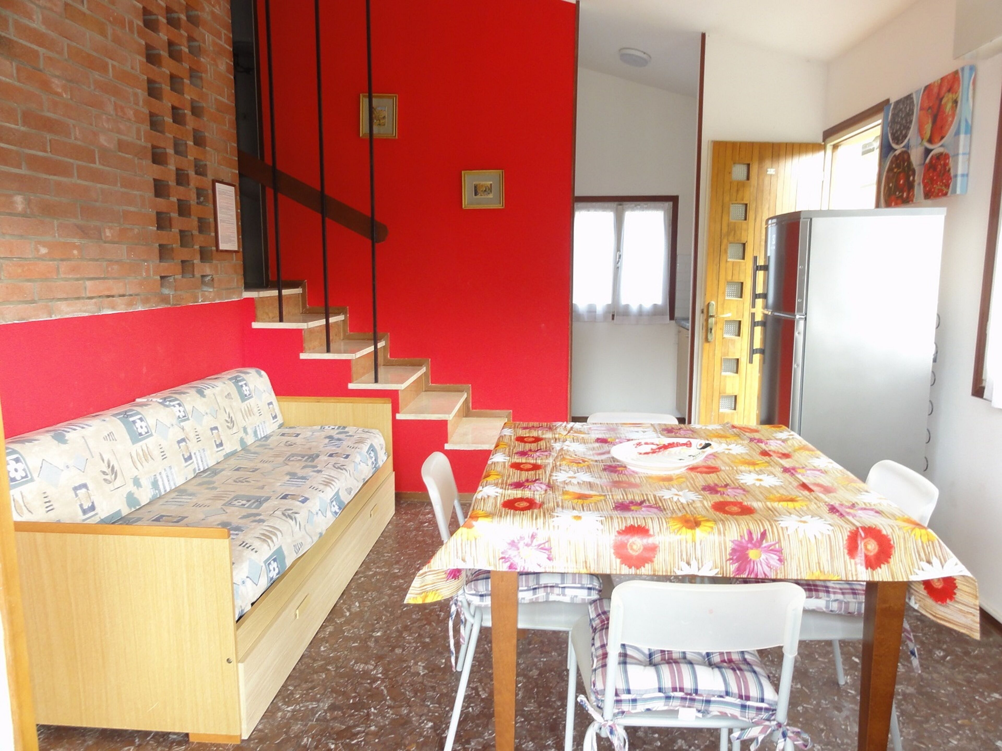 A dining area with a table, chairs, and a sofa. There is a staircase leading to another room.