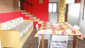 A dining area with a table, chairs, and a sofa. There is a staircase leading to another room. - Villa Letizia (San Michele al Tagliamento)