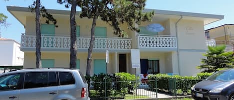 A two-story building with a balcony, a sign indicating 'LIVENZA', and a parked car in front.