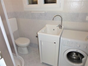 Casa de banho compacta com sanita, lavatório e máquina de lavar roupa.