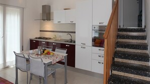 Cozinha moderna com armários brancos, uma mesa de jantar com cadeiras e uma escada com corrimão de madeira.