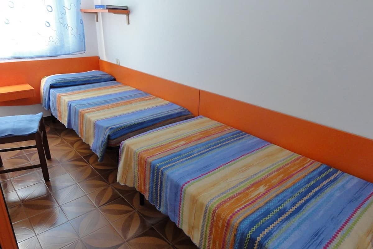 Una habitación tipo dormitorio con tres camas dispuestas a lo largo de la pared, una mesita pequeña y una silla.