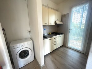 A compact kitchen with a washing machine, a gas stove, and a window with patterned curtains.