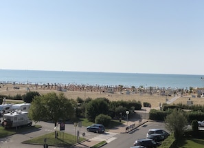 A beach with numerous umbrellas and tents, a parking area with RVs, and a clear view of the sea.