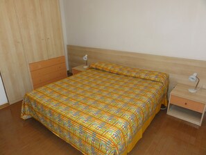 A bedroom with a bed, two bedside tables, a nightstand, a wardrobe, and a mirror.