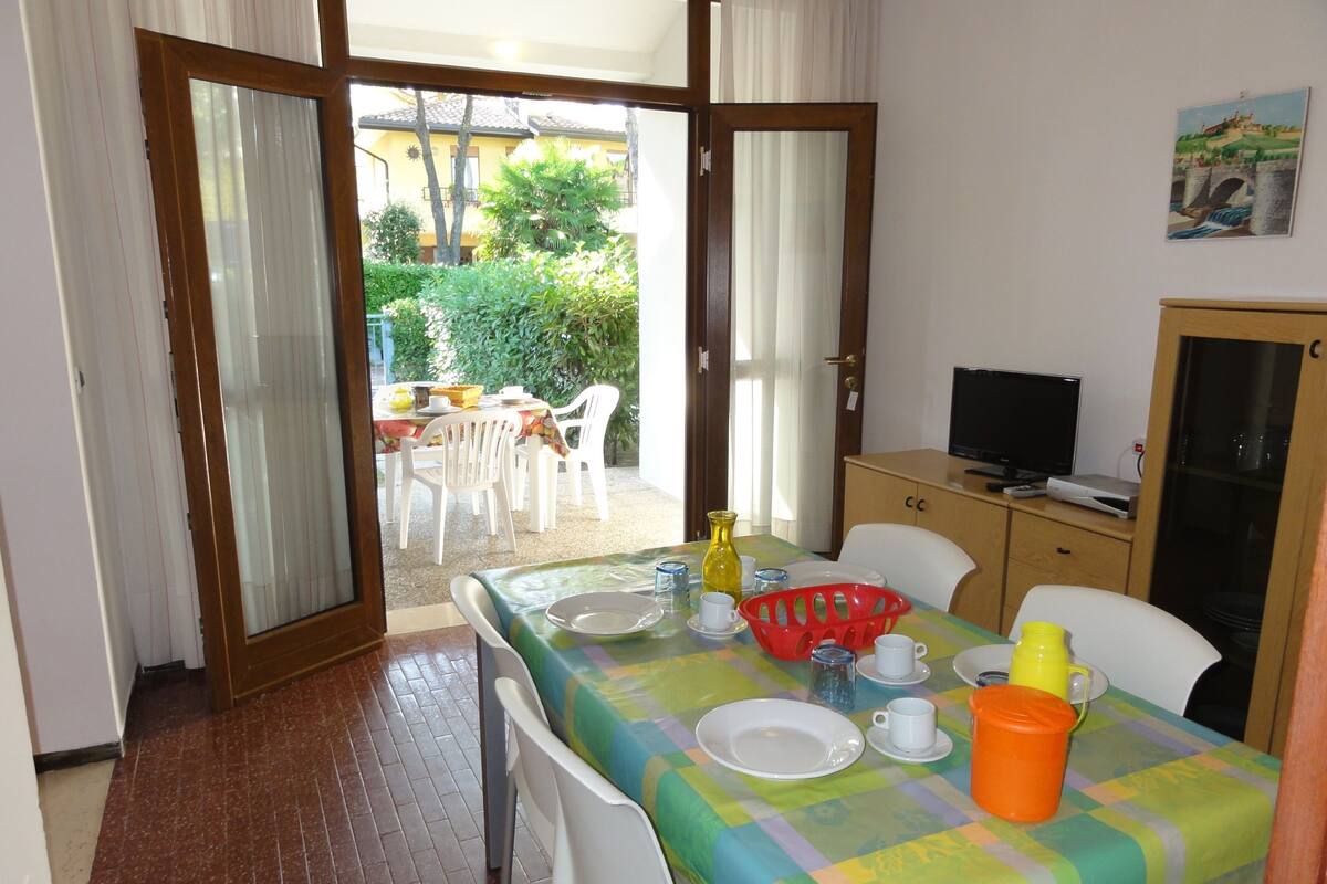 A dining area with a table set for two, chairs, a television, and a cabinet.