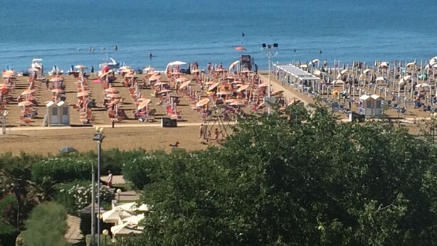 Ein Strand mit vielen Sonnenschirmen und Liegestühlen, der auf ein Strandhotel hindeutet.