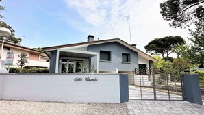 Villa Wanda, una villa moderna con entrada protegida por un portón, camino de entrada cubierto y un letrero que indica un restaurante.