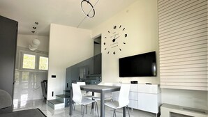 Una cocina moderna con comedor, un reloj grande y un televisor de pantalla plana.