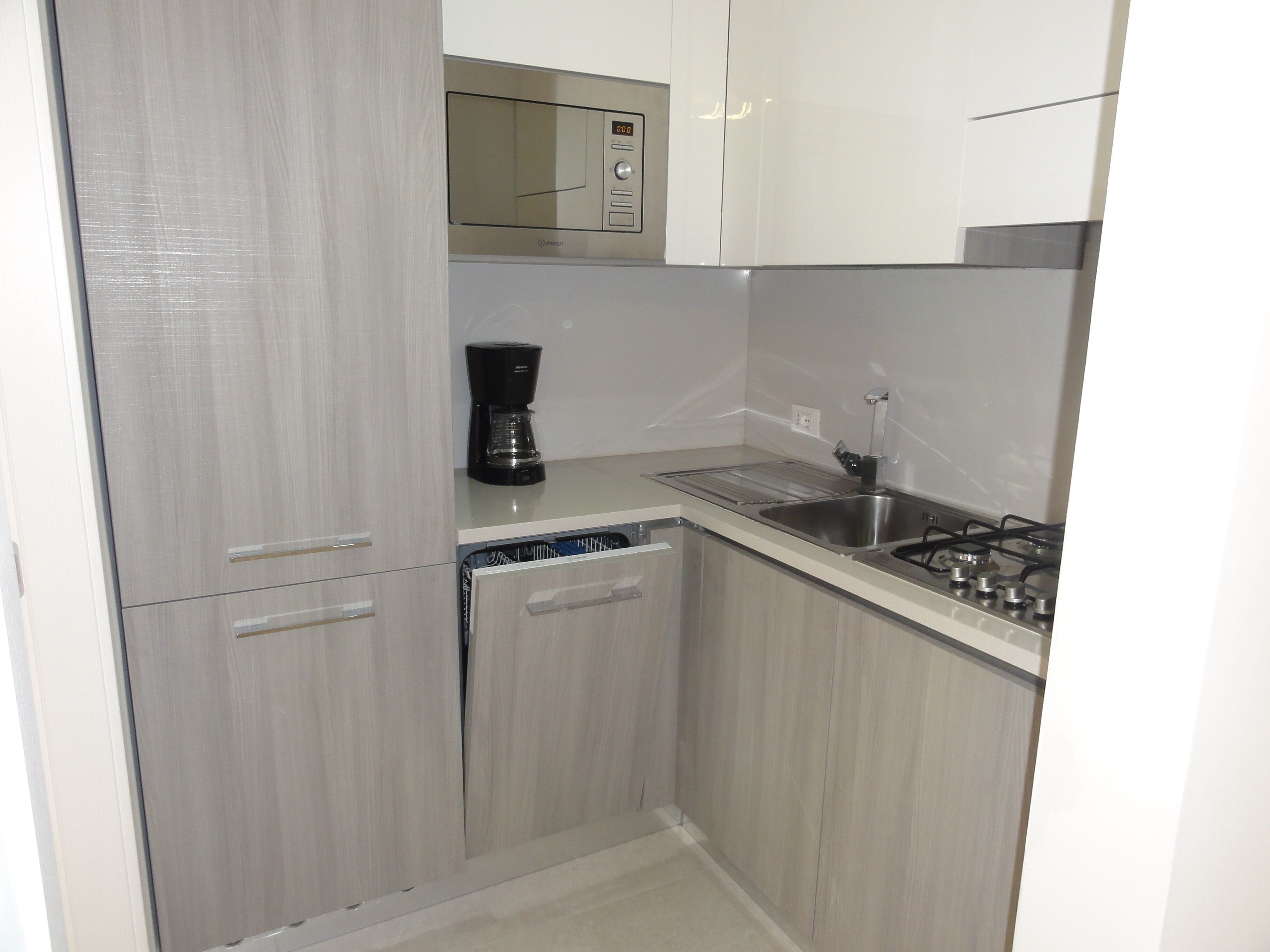 A compact kitchen with a microwave, coffee maker, dishwasher, and gas stove.