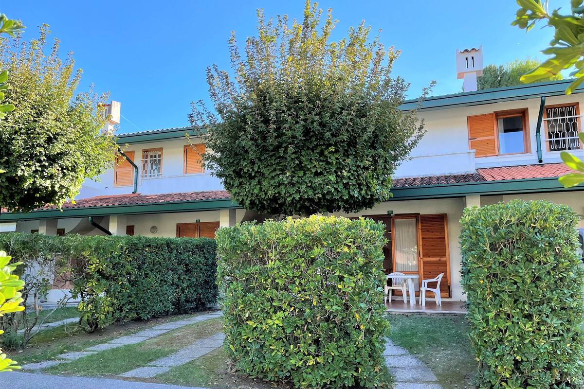 A building with a tiled roof, a covered patio with outdoor furniture, and well-maintained hedges.