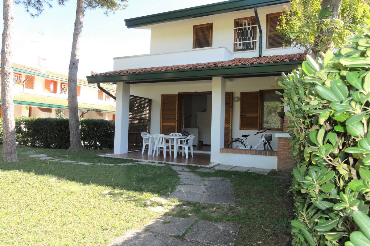 A two-story house with a patio area, a dining table with chairs, and a bicycle parked outside.