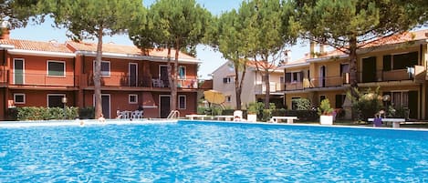 Area piscina con diversi edifici, posti a sedere all'aperto e alberi.
