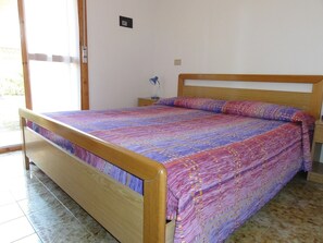 A single-bed room with a wooden frame, a patterned bedspread, a nightstand, and a power outlet on the wall.
