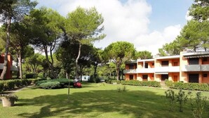 A courtyard with a lawn, trees, and a building with multiple balconies. - Villaggio White Star (San Michele al Tagliamento)