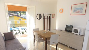 Un espacio habitable compacto con sofá, mesa de comedor, sillas, zona de cocina con microondas y balcón con mobiliario exterior.