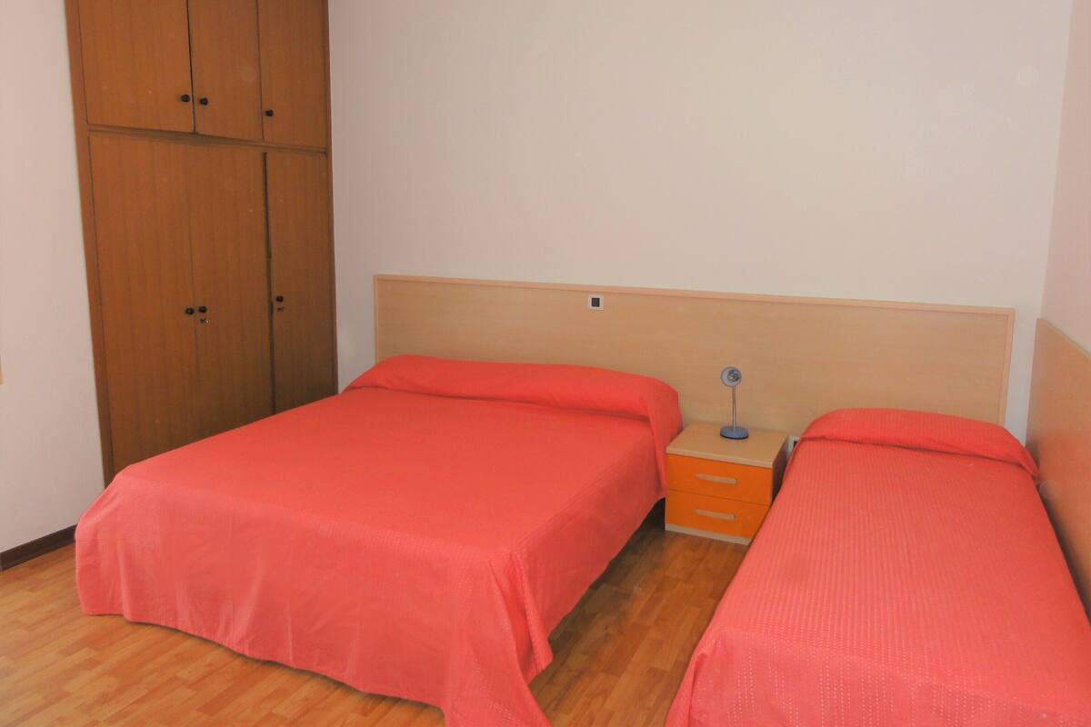 Una habitación con dos camas individuales, un armario de madera y una mesita de noche con lámpara.