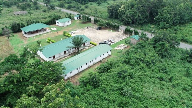 An aerial view of a property with multiple buildings, including a large rectangular structure with a green roof, smaller buildings with green roofs, and a parking area.