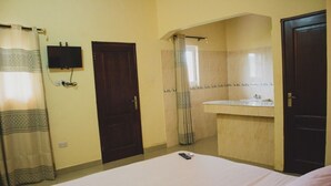 A bedroom with a bed, a TV mounted on the wall, a bathroom with a sink, and two doors.