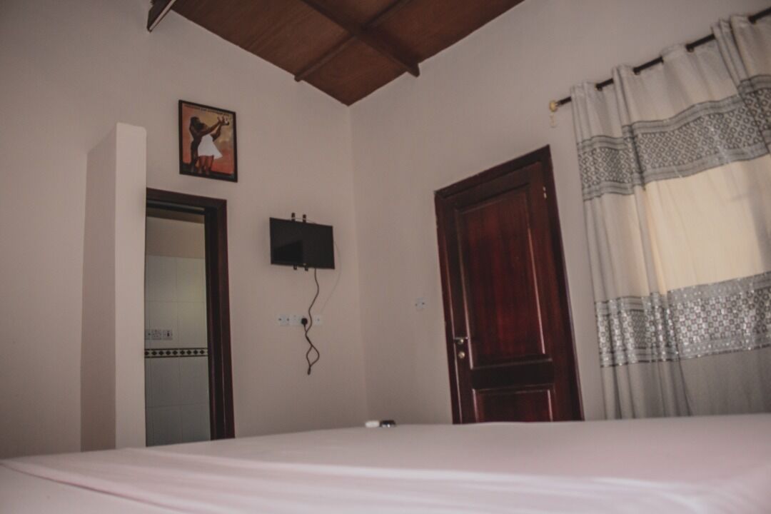 A bedroom with a bed, a wooden door, a wall-mounted TV, and a framed picture.
