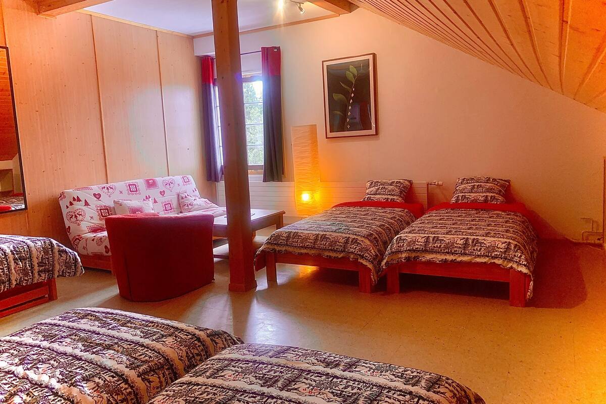 Un dormitorio acogedor con techo inclinado, estructura de cama de madera, una silla roja y un sofá estampado.