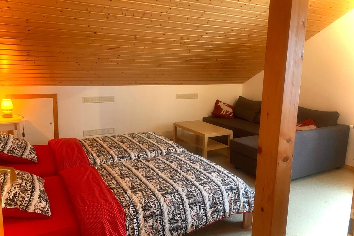 Una habitación acogedora con techo de madera, cama con ropa de cama estampada, una mesita y un sofá.