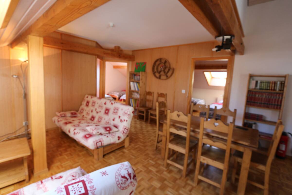 Una sala de estar acogedora con techo de madera, un sofá, una mesa de comedor con sillas y una estantería.