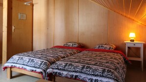 A room with two beds, wooden walls, a small bedside table with a lamp, and a door with a handle. - La Maison de la Montagne (Ollon)