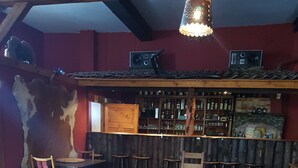 A wooden dining table with benches, a bar area with shelves of bottles, and a rustic decor including a large animal hide on the wall.