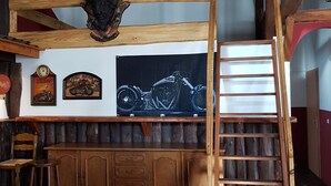 A rustic bar area with wooden beams, a motorcycle poster, and a wooden ladder.