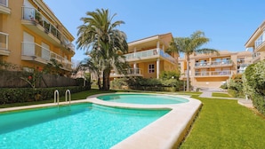 Una piscina rodeada de un césped cuidado y palmeras, con edificios altos al fondo.