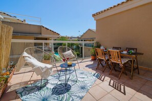 A patio with a table, chairs, a hammock, and a view of a swimming pool and neighboring buildings.